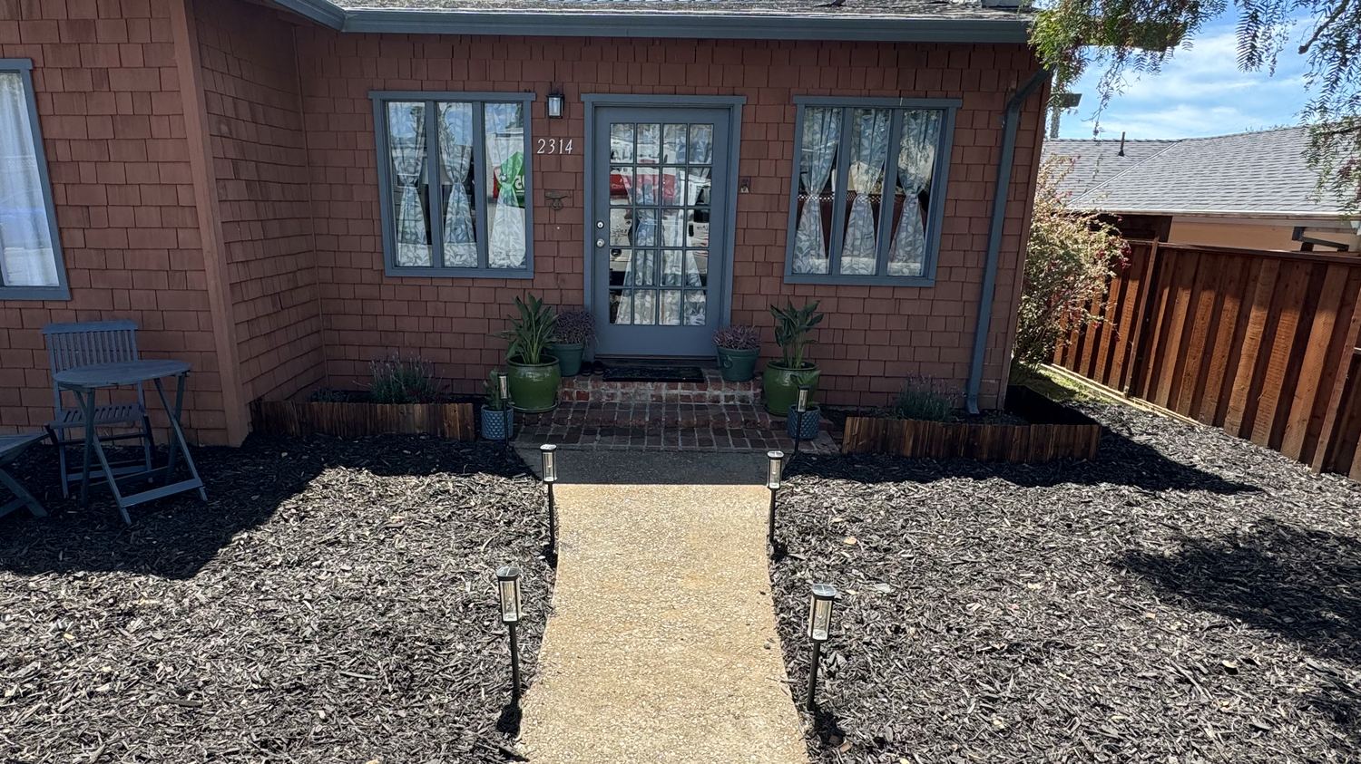 The same front yard after: dark mulch beds either side of the walkway, planted borders along the house.