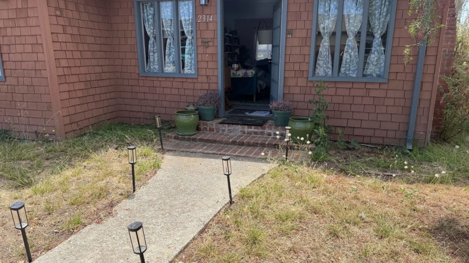 A front yard before work: dry patchy grass and weeds on both sides of the walkway.
