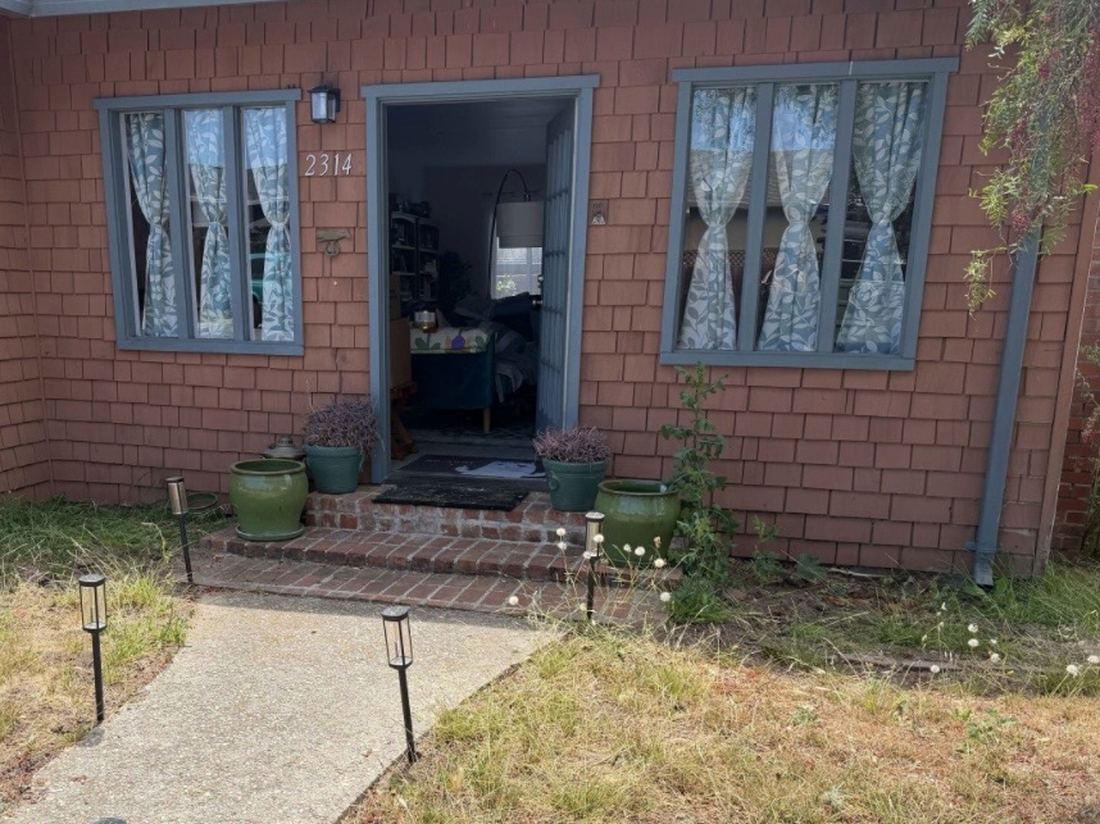 A front entry with dead grass and weeds growing up against the house.