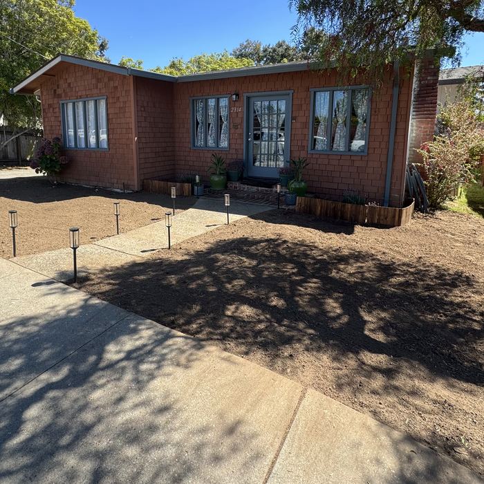 A front yard graded to bare soil with path lights installed, ready for mulch.